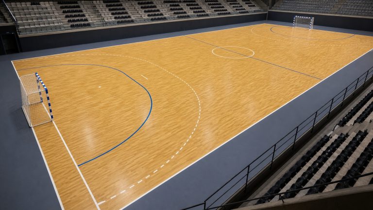 Vue panoramique photoréaliste d’un terrain de handball intérieur avec buts et marquages réglementaires visibles.