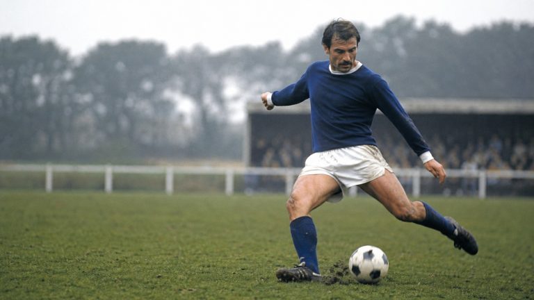Défenseur de football en maillot bleu sur un terrain breton, dans une ambiance de match en Côtes-d’Armor.